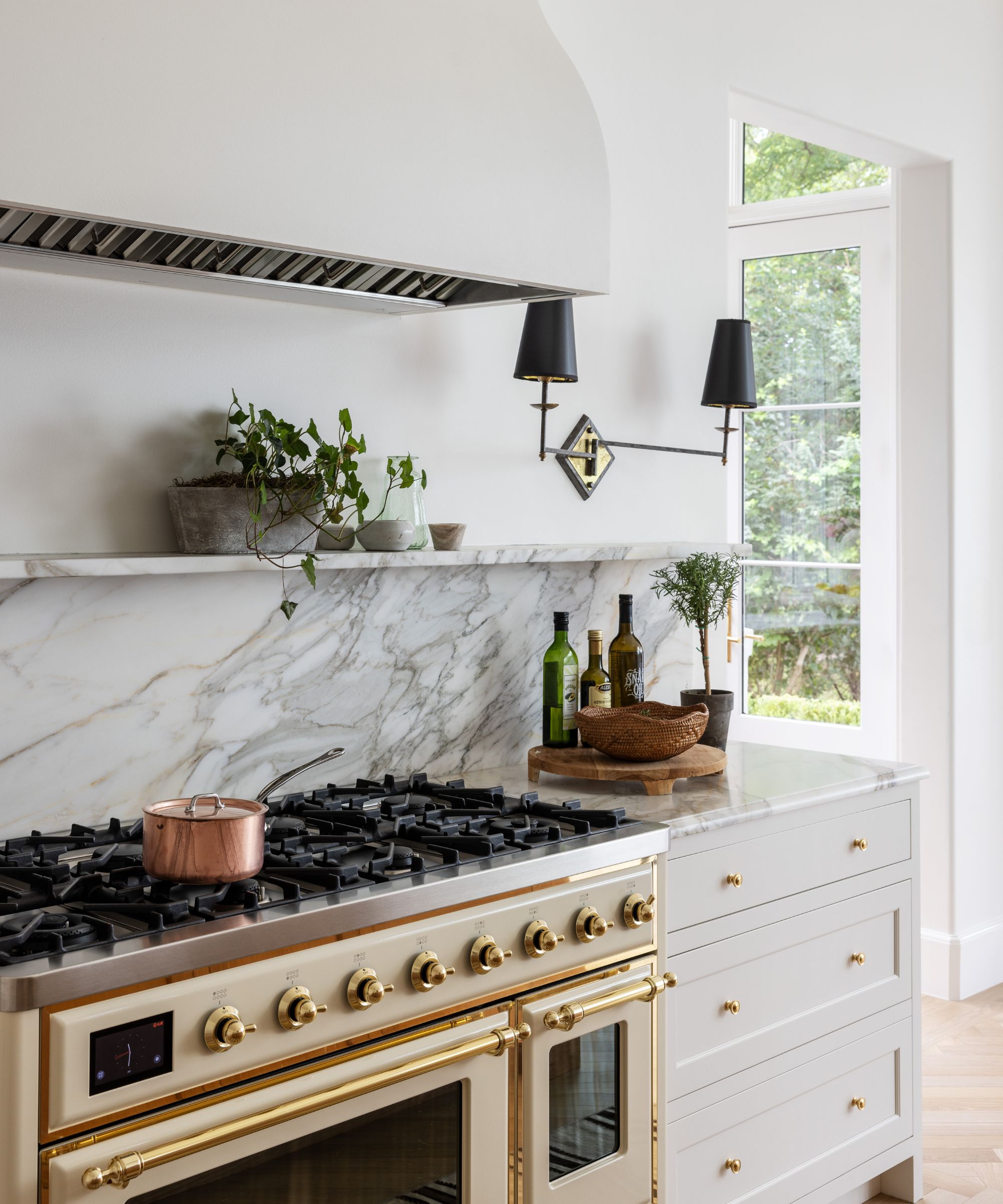 A white kitchen with marble countertops. a white and brass range cooker, and vintage wall lights