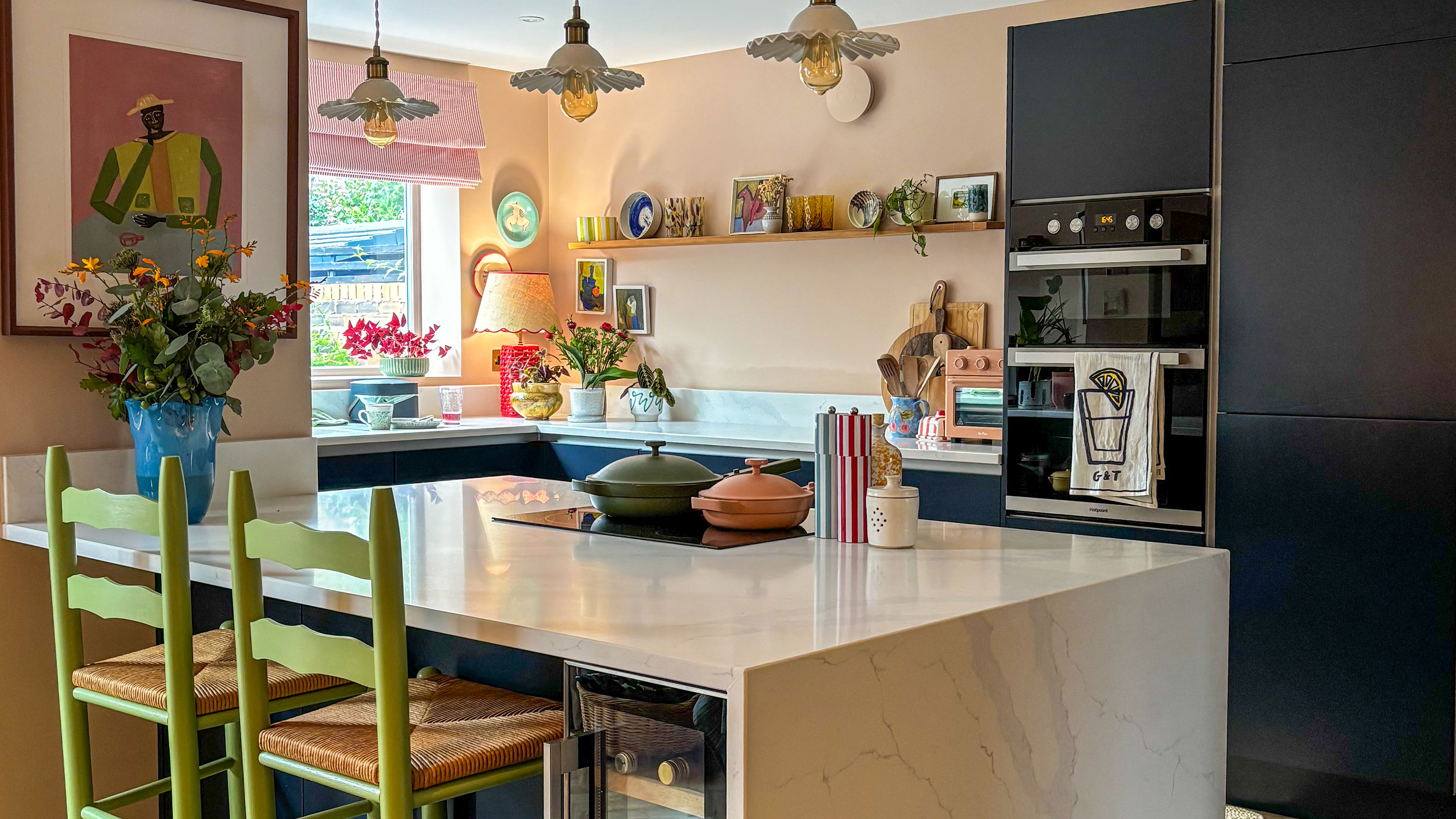 Kitchen with marble effect waterfall island, holding wine fridge, with two green bar stools, topped with three pendant lights