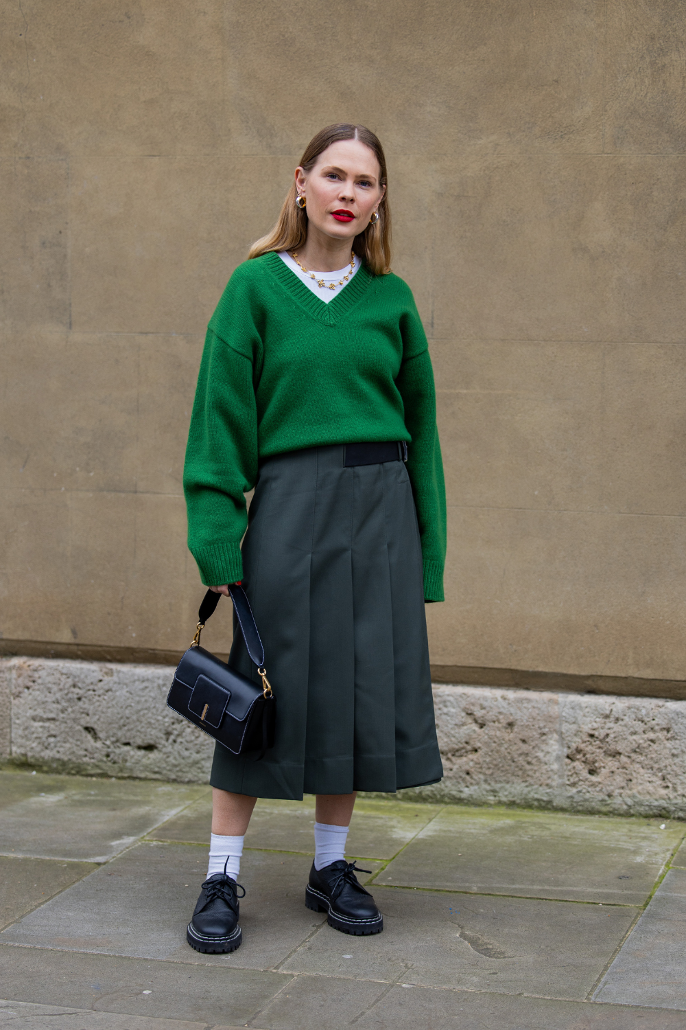 Jessie Bush wears green v neck jumper, high waisted skirt, black bag outside Huishan Zhang during London Fashion Week