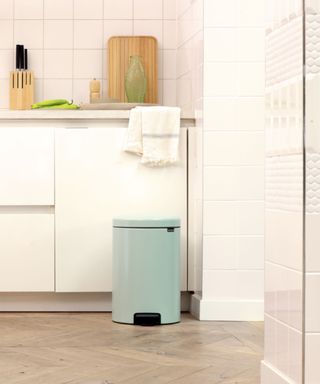 Green trash can with lid and foot pedal in white kitchen