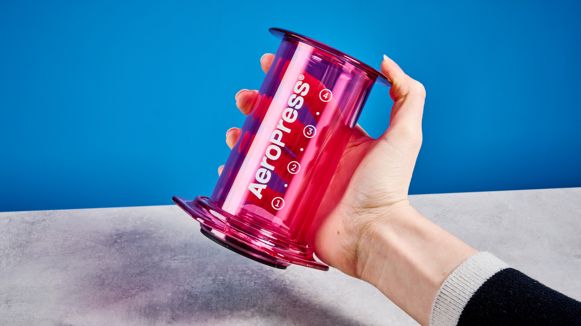 the aeropress clear color in pink photographed against the blue tom's guide background