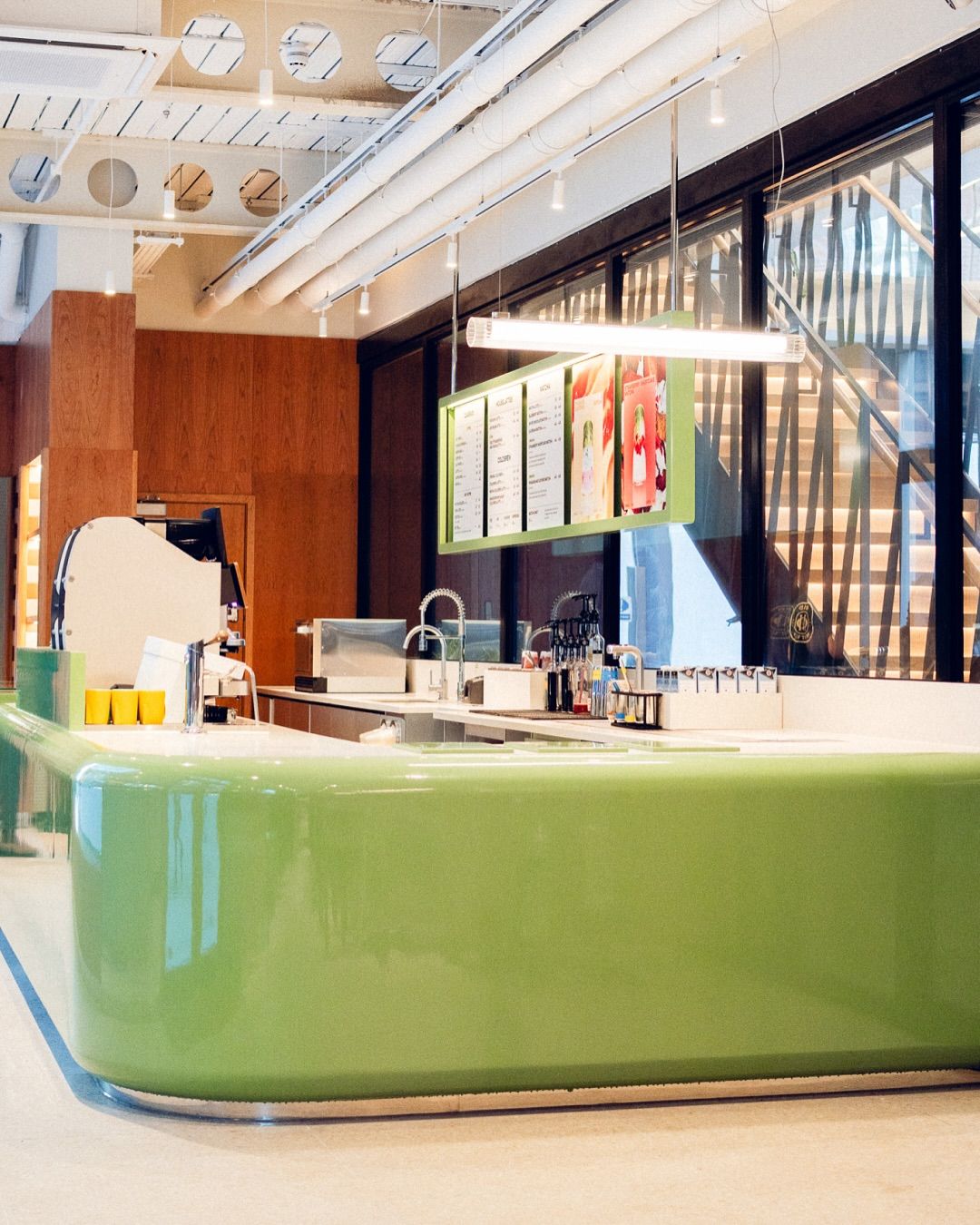A Space Age-inspired matcha cafe with vivid furnishings, lacquered green bar counters, glass block walls, and wooden decor.