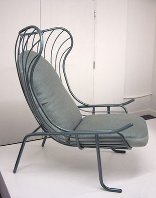 A curved shair with metal skeleton base and grey upholstery seat. Displated and photographed on a white platform