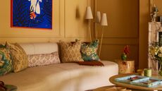 a yellow living room with a curved sofa, a three pronged floor lamp, and bright blue artwork
