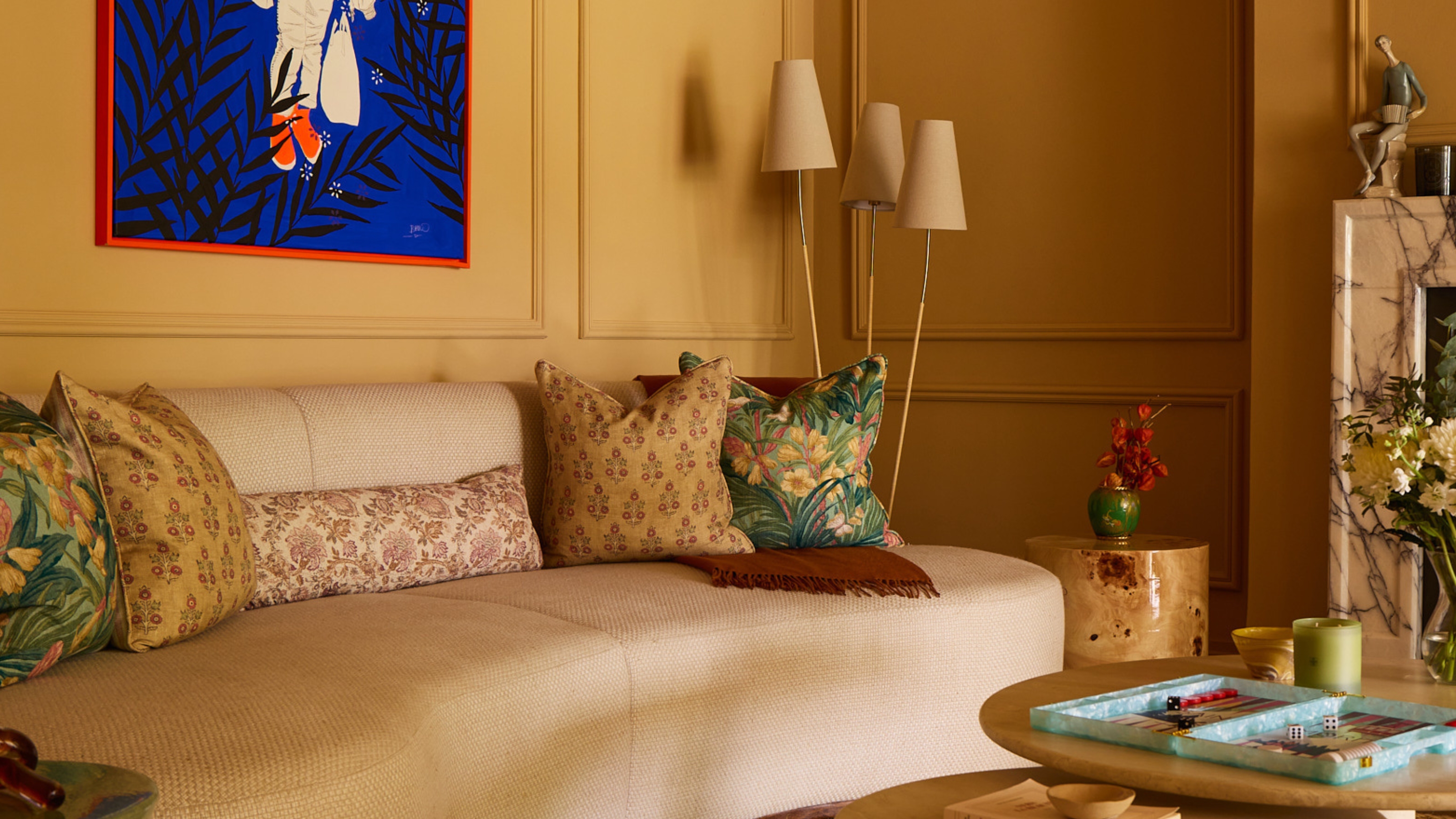 a yellow living room with a curved sofa, a three pronged floor lamp, and bright blue artwork