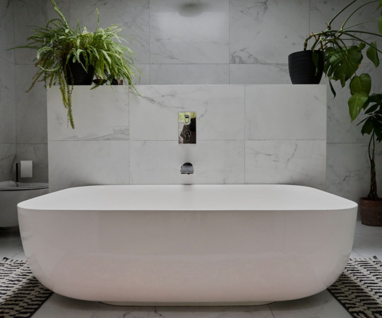 A white bath and white porcelain tiled wall with a faucet in built into the wall