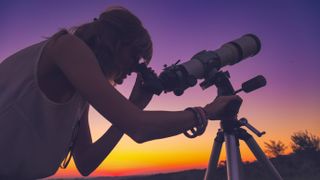 Girl looking through telescope on tripod at sunset