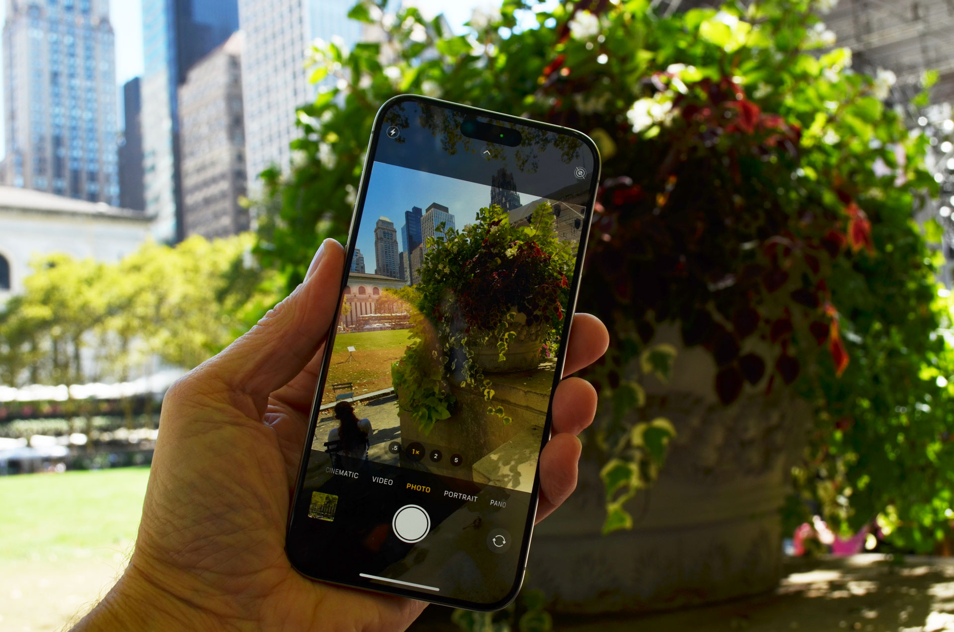 Apple iPhone 15 Pro Max i hånden med buske i baggrunden.