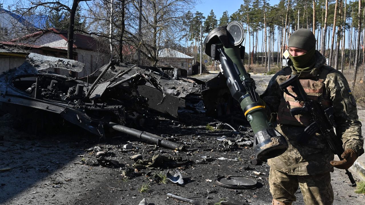 A Ukrainian soldier poses with an NLAW next to a destroyed Russian tank