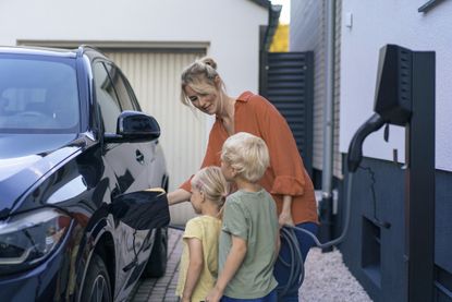 Woman charging electric car in front of children