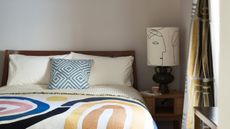 Cream guest bedroom with colorful throw and bedside lamp with modern print