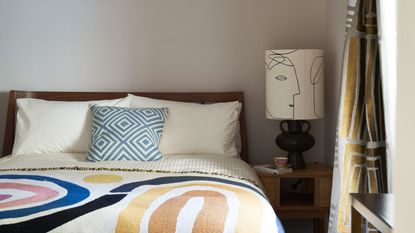 Cream guest bedroom with colorful throw and bedside lamp with modern print