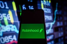 Green Robinhood logo on smartphone with stock charts blurred in the background