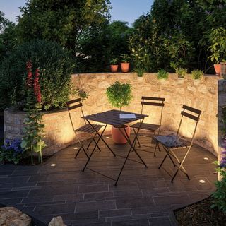 a wooden dining set with a lit-up brick wall, one of our favorite garden lighting ideas