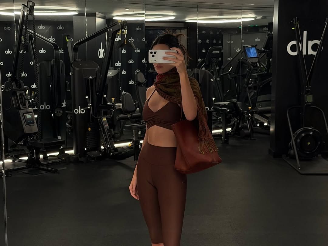 kendall wears a brown scarf, brown sports bra, brown capri leggings, and a brown leather bag.