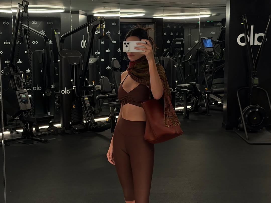 kendall wears a brown scarf, brown sports bra, brown capri leggings, and a brown leather bag.