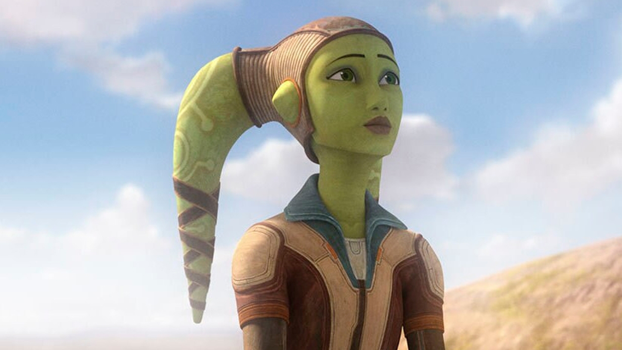 Hera Syndulla is a green-skinned Twi'lek with two head tails (known as lekku) protruding from the top left and right of her head. She is wearing a brown leather cap and a brown and cream leather jacket. She is looking off into the distance. Behind here is a light blue cloudy sky.
