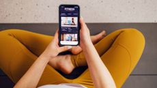 Woman's hands using one of the best workout apps, sitting on yoga mat and wearing workout clothes 