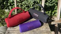 Two JBL Charge 6 speakers and one Flip 7 speaker grouped together on garden chair