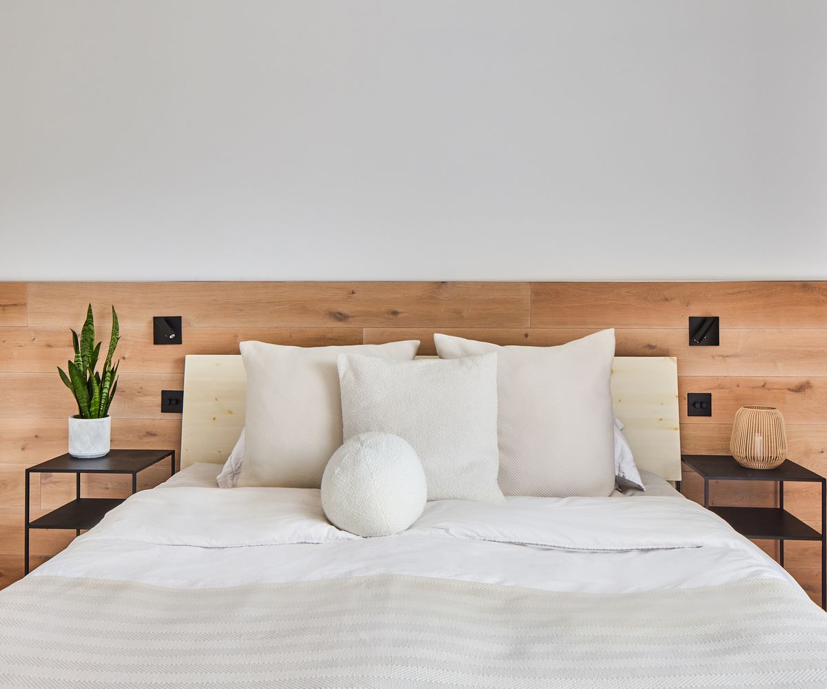 A double bed in front of a wooden wall panelling with white bed clothes and black side tables
