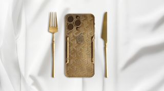 A gold-covered chocolate bar in the shape of the Apple iPhone 15 Pro Max with a gold knife and a fork