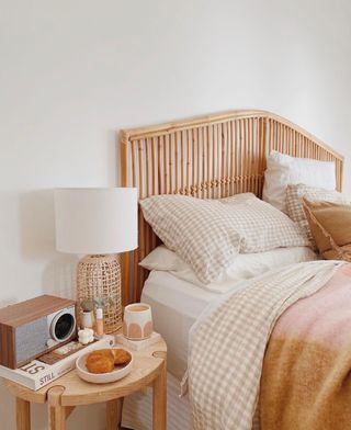 Cozy layered bedding in warm colors on rattan bed frame with a round wooden bed table
