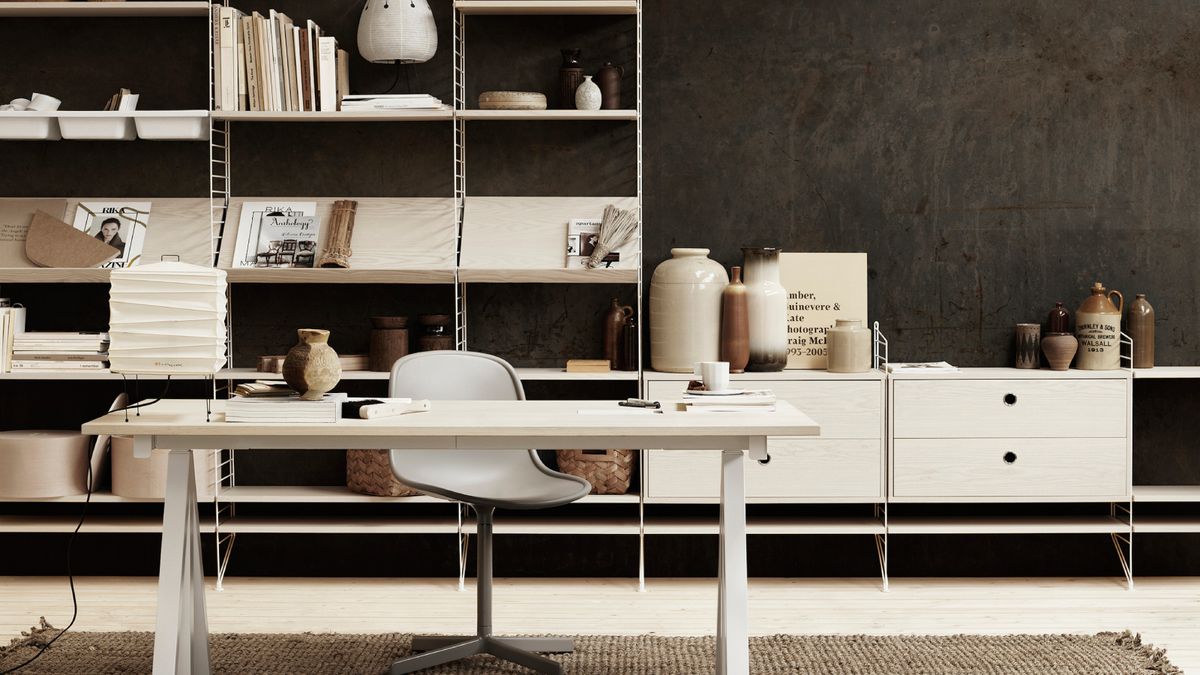 home office with white string shelving unit on black wall with white desk and chair in front