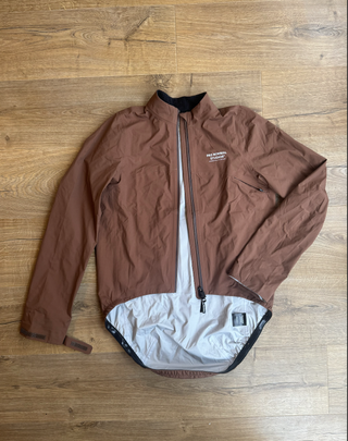 A flat lay of the pas normal jacket in brown with a silver inner lining.