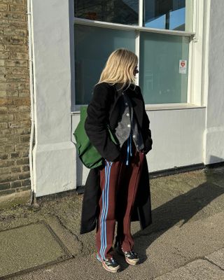 Woman wears Wales Bonner x Adidas track pants, a grey cardigan, Salomon sneakers and a black coat.