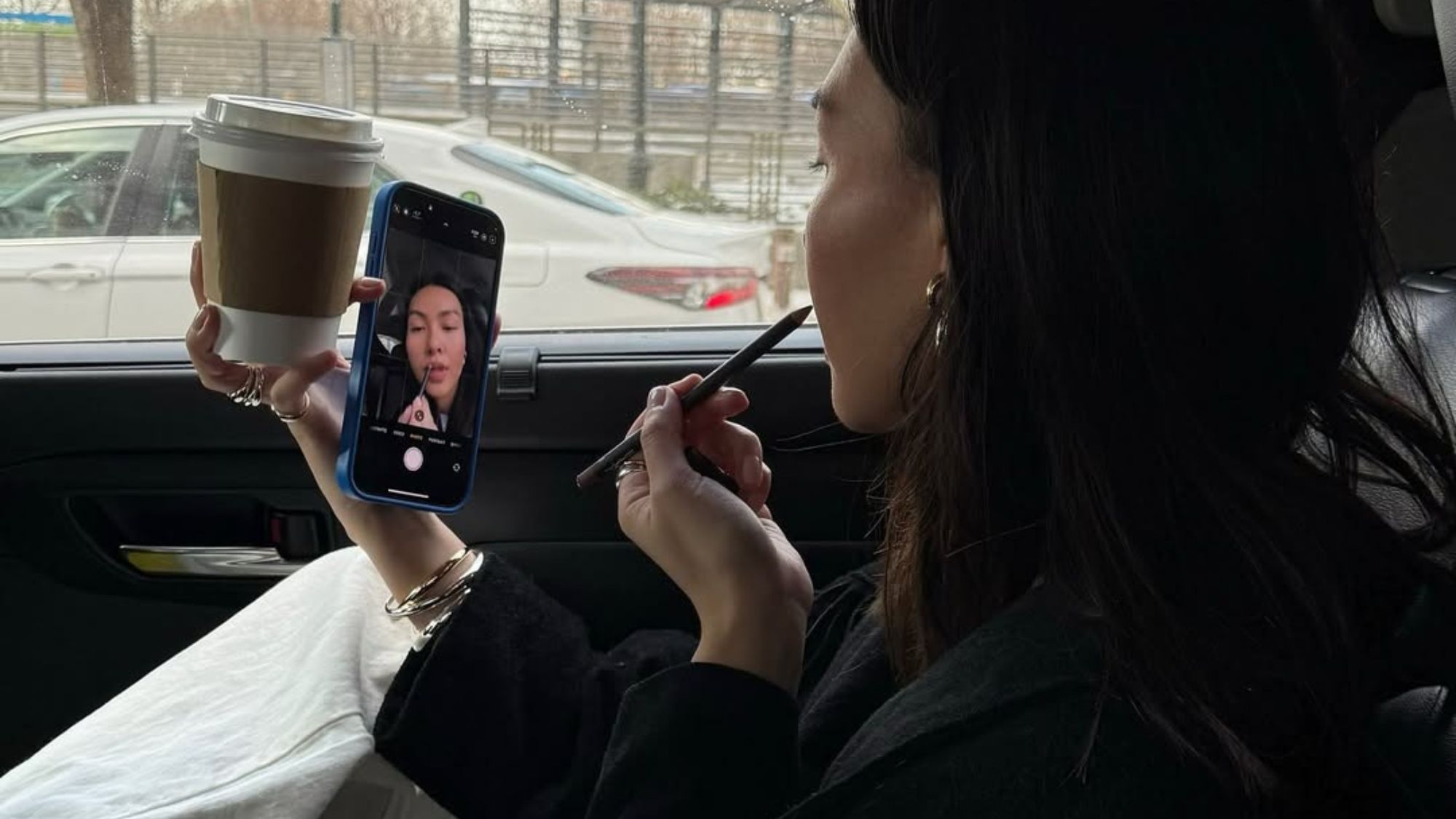 A woman applying lip liner in the car.