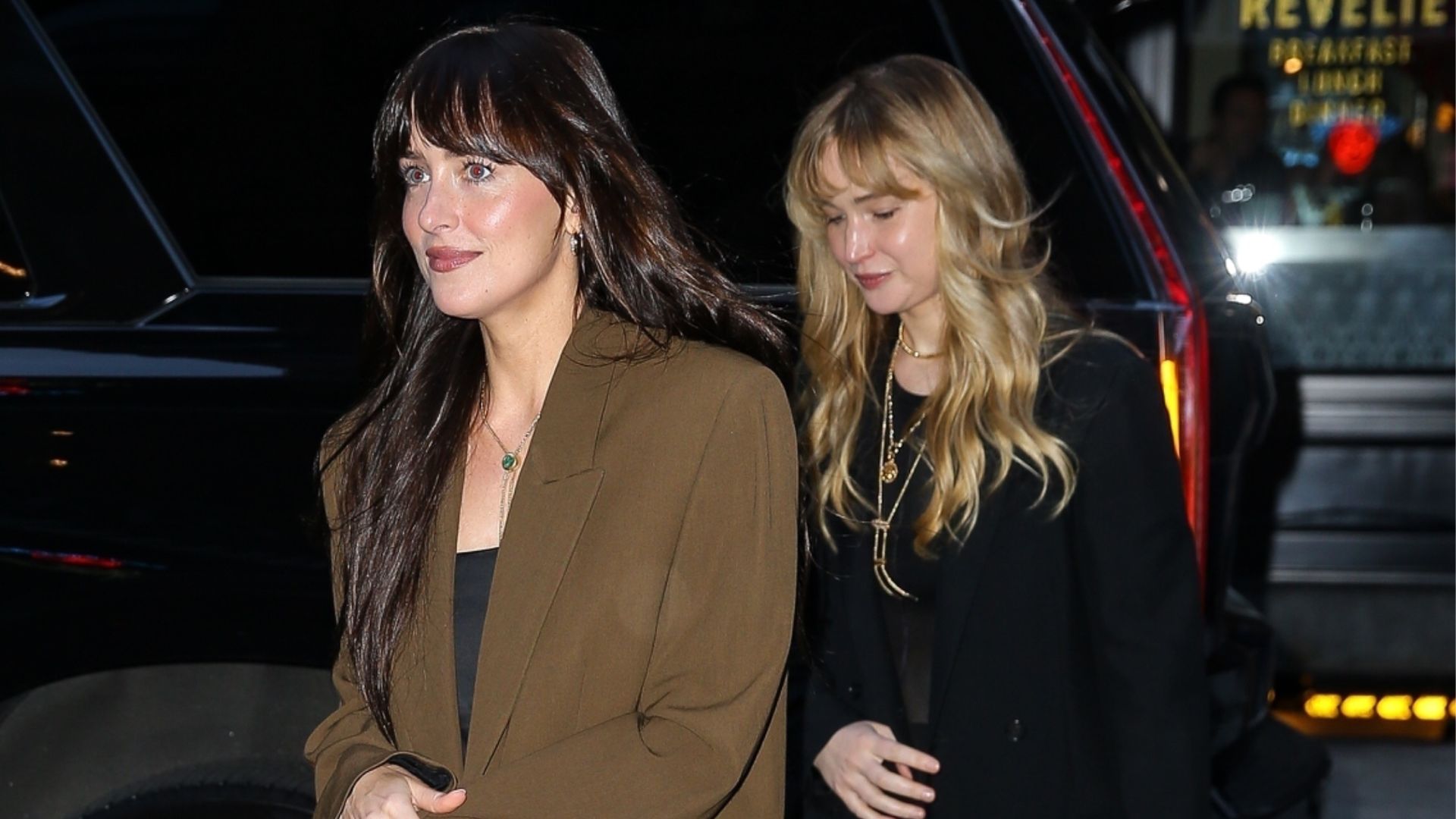 Dakota Johnson walks in front for Jennifer Lawrence wearing wide-leg trousers with loafers. Lawrence walks behind wearing wide-leg trousers with full-coverage ballet flats.