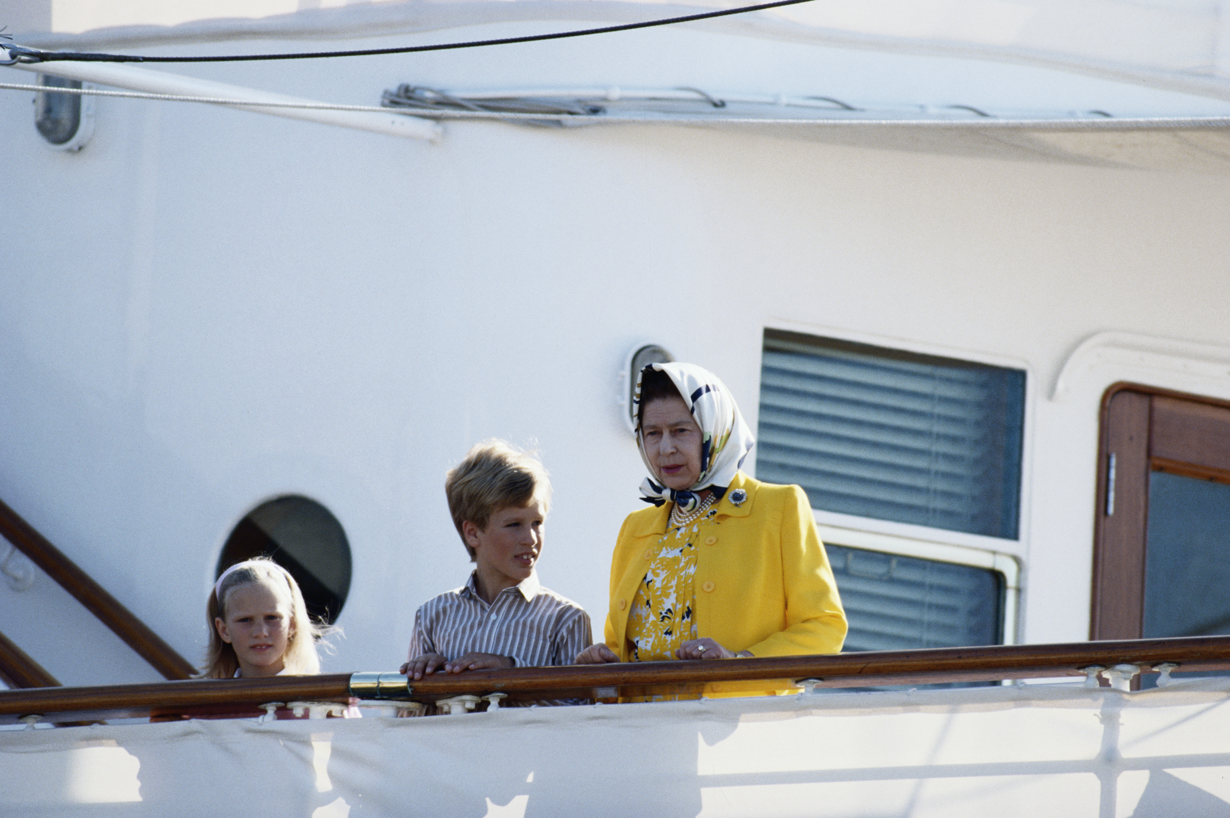 Queen Elizabeth standing with Zara Tindall and Peter Phillips on the Royal Yacht Britannia