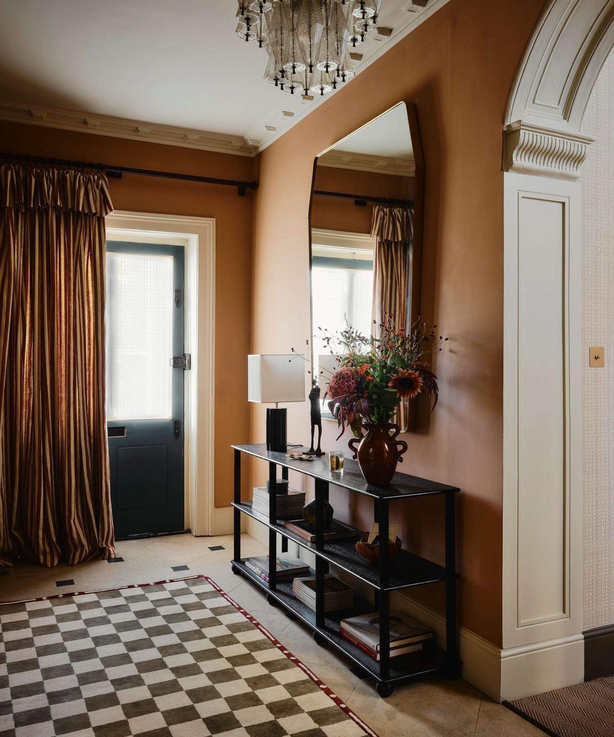 warm ochre hallway with tiled floor, checkerboard rug, large mirror and console table vignette and a striped frilled front door curtain