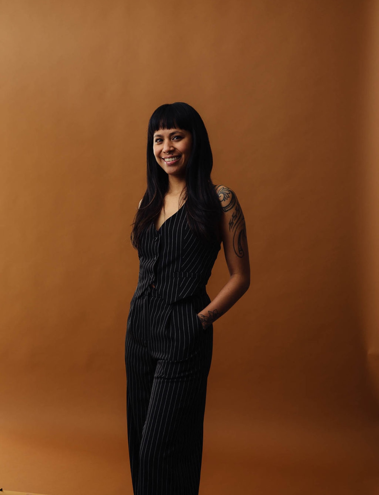 a woman with tattoos and dark hair with bangs in a pinstripe outfit