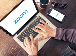 Someone loading Zoom on a laptop and a phone 