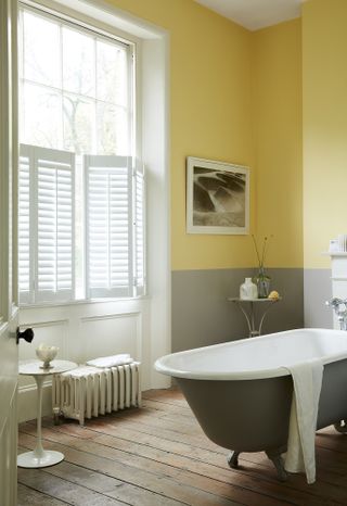 Yellow and grey bathroom with white plantation shutters and freestanding bath