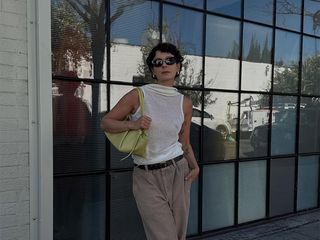 Alyssa wears white open back top, baggy trousers, light green handbag, sunglasses, and earrings.