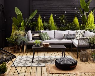 botanical style patio with a lush backdrop of foliage planting and gray corner sofa with patterned cushions and rug