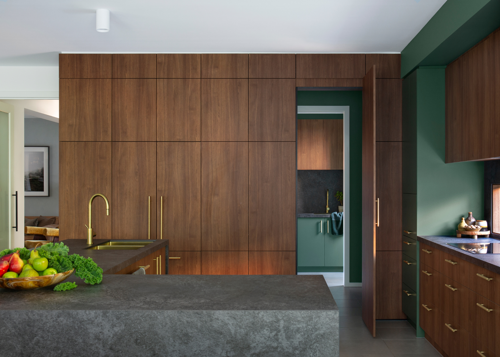 A dark wood and green kitchen with a dark gray island and brass fixtures and fittings