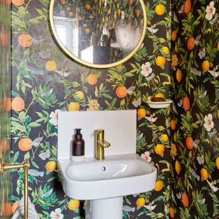 Cloakroom with white basin and bold, citrus fruit-patterned wallpaper