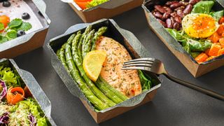 Boxes of healthy food, including box of salmon fillet and asparagus with lemon slice, another with red kidney beans, lettuce, half a soft-boiled egg and cubes of butternut squash