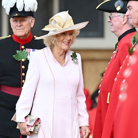 Queen Camilla wearing a pink coat and hat standing with Chelsea pensioners