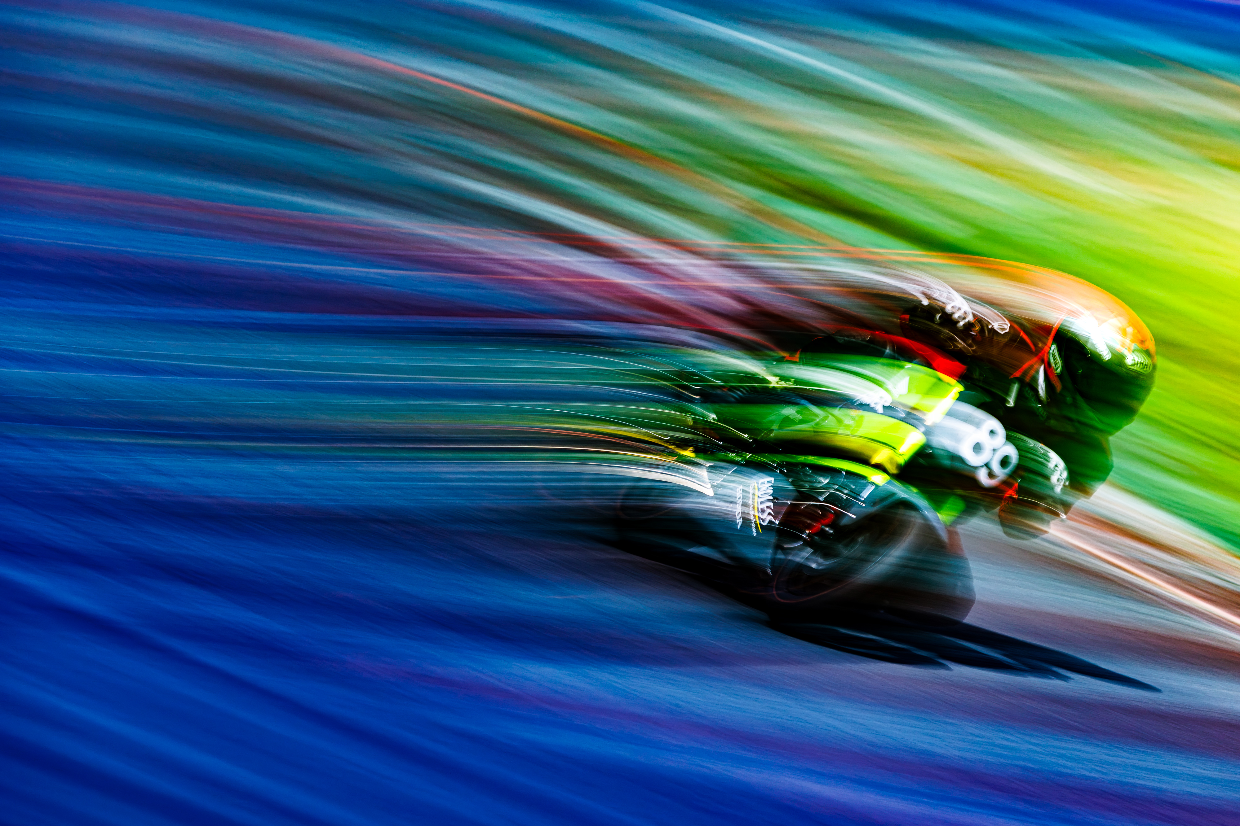 A blurred, high-speed image of a race car, with a rainbow-like streaking of colors in the background, gives the impression of extreme motion.