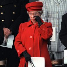 Queen Elizabeth wearing a red coat and hat wiping her eye