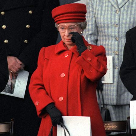 Queen Elizabeth wearing a red coat and hat wiping her eye