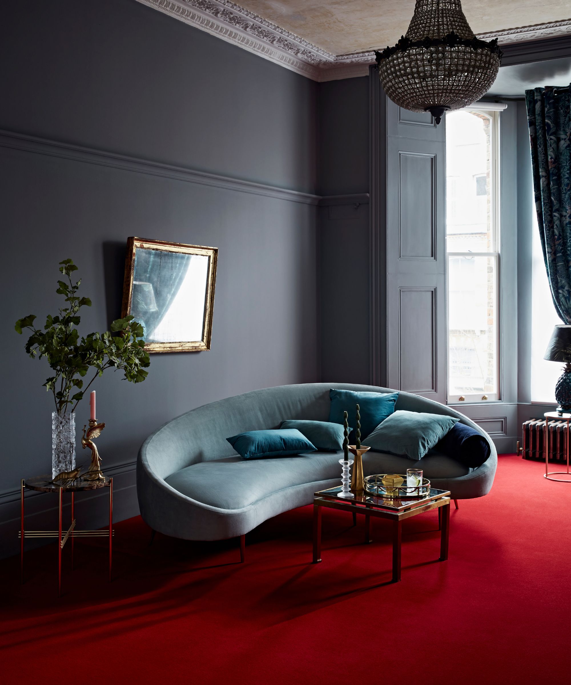 dark grey traditional victorian living room with a red carpet and a curved velvet couch and a large crystal vintage chandelier above