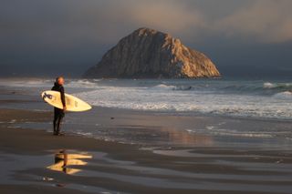 A male surfer gets ready to enter the water at Morro Strand State Beach in Morro Bay, California