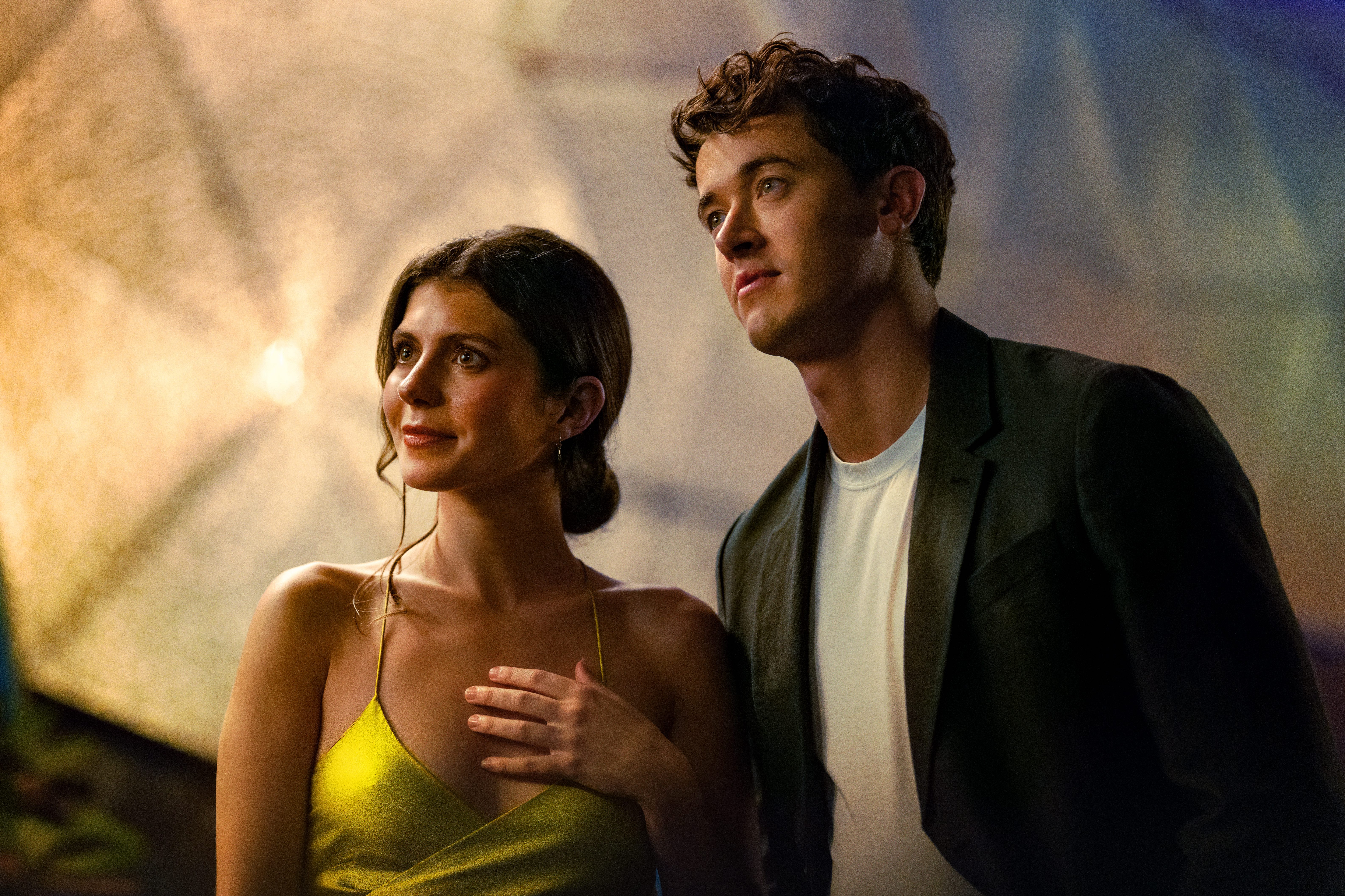 Emily Bader as Poppy wearing a bright yellow dress and Tom Blyth as Alex wearing a black blazer and white tshirt in People We Meet on Vacation