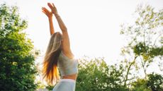 Woman doing wall angels in the garden wearing activewear among trees and sunshine
