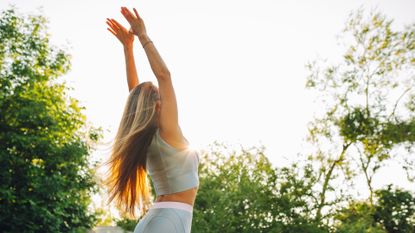 Woman doing wall angels in the garden wearing activewear among trees and sunshine